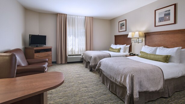 Une chambre d’hôtel avec deux lits, un bureau, une télévision et une fenêtre avec des rideaux.