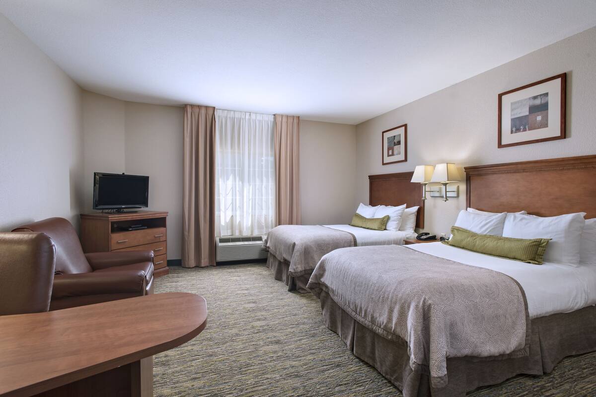 Een hotelkamer met twee bedden, een bureau, een televisie en een raam met gordijnen.