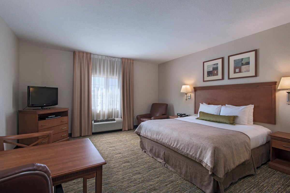 Een hotelkamer met een bed, een televisie, een bureau, een stoel en een raam met gordijnen.