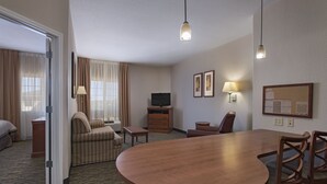 Une chambre d’hôtel avec une table à manger en bois, deux chaises, un canapé, une télévision, un bureau et une lampe.