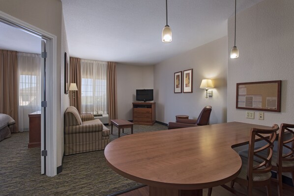 Habitación de hotel con una mesa de comedor de madera, dos sillas, un sofá, un televisor, un escritorio y una lámpara.