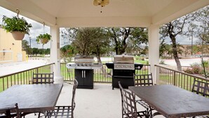 Une terrasse extérieure avec une table et des chaises, un barbecue et des plantes suspendues.