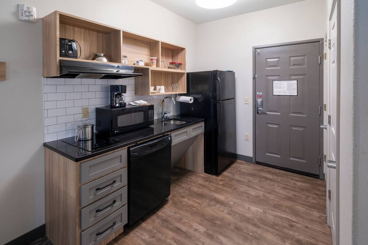 Eine kompakte Küche mit Mikrowelle, Toaster und Kaffeemaschine auf der Arbeitsplatte, einem Geschirrspüler und einem Kühlschrank.