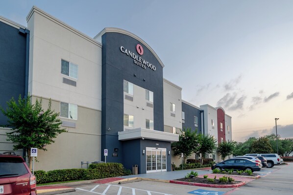 Un hotel con fachada moderna, un letrero llamativo de Candlewood Suites y un estacionamiento con varios autos.