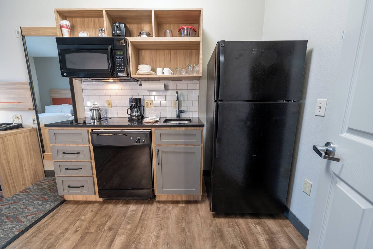 Eine kleine Küche mit Mikrowelle, Kaffeemaschine, Spüle und einem schwarzen Kühlschrank.