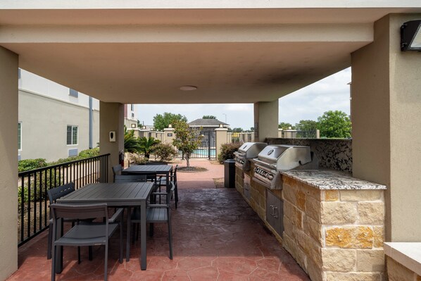 Une terrasse extérieure dotée d’un barbecue et d’un espace repas, entourée de murs en pierre et offrant une vue sur les bâtiments voisins.