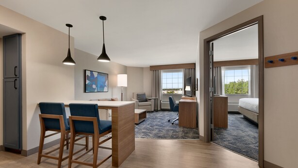 Une chambre d’hôtel équipée d’une kitchenette, d’un bureau, de deux chaises, d’un lit et d’une grande fenêtre.