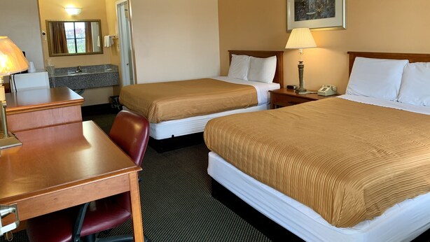 A hotel room with two beds, a desk, a chair, a lamp, a phone, and a painting on the wall. - Regency Inn Fairfield (Fairfield)