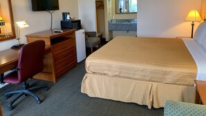 A hotel room with a bed, desk, chair, television, and a bathroom with a sink and mirror. - Regency Inn Fairfield (Fairfield)