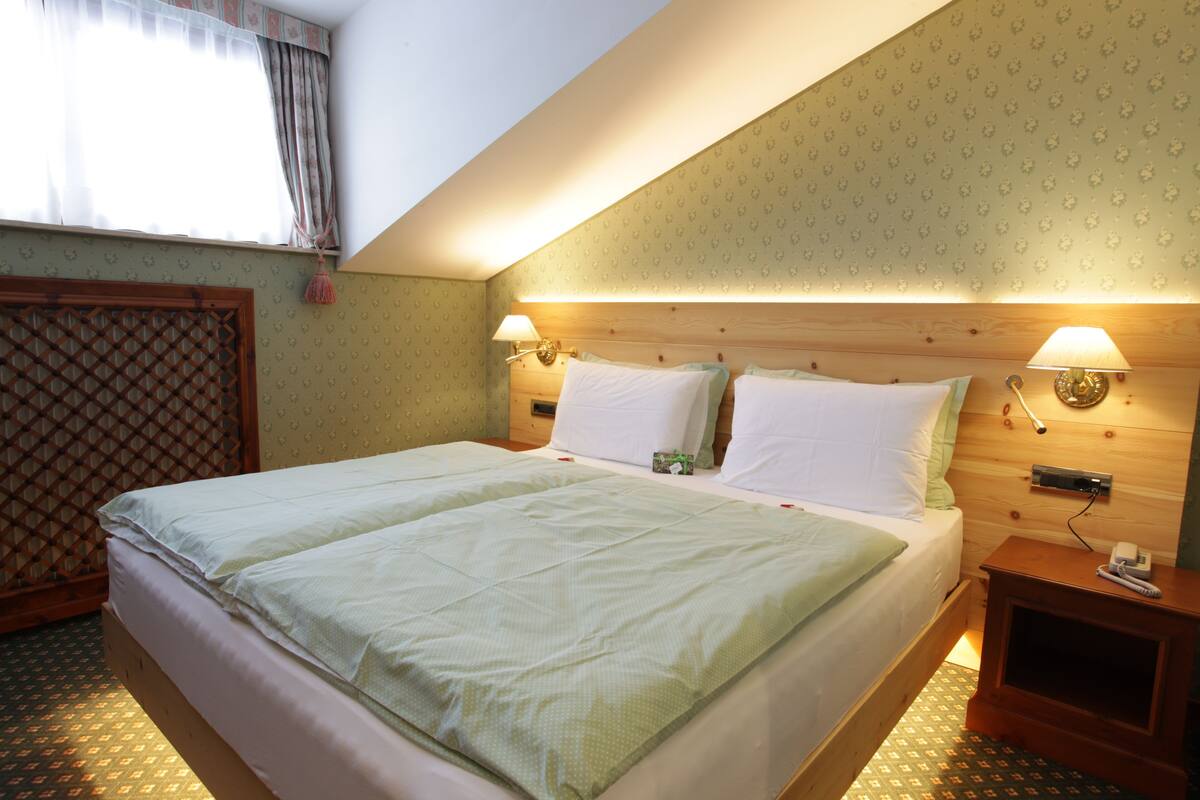 A hotel room with a large bed, two bedside lamps, a wooden headboard, and a patterned wall.