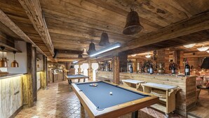 Une table de billard avec une boule blanche, des tables en bois et un coin bar avec des bouteilles.