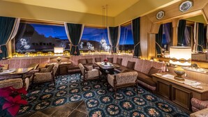 Un espace salon confortable, avec un canapé, des fauteuils et une table, agrémenté d’un tapis à motifs et de grandes fenêtres avec des rideaux.