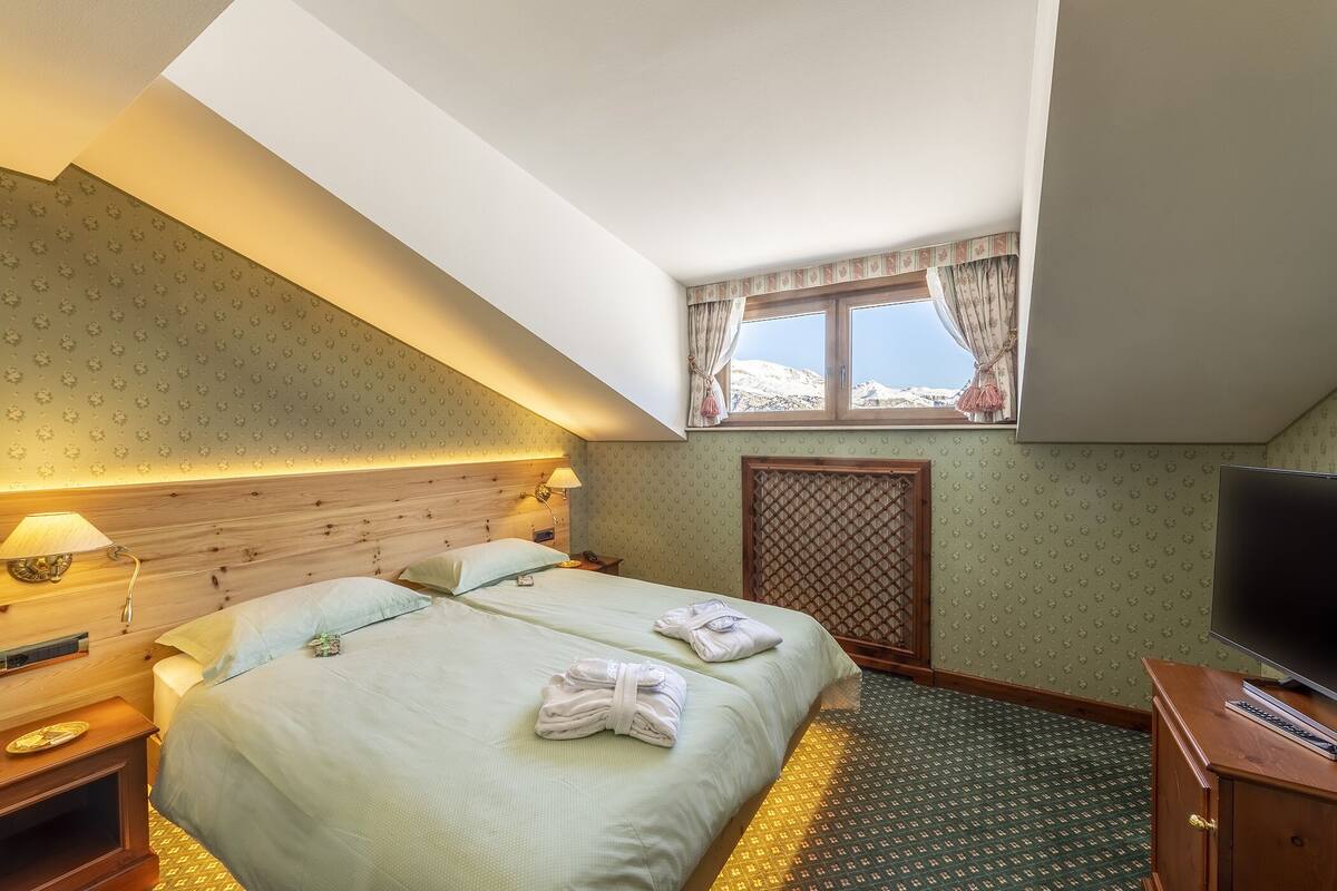 A hotel room with a bed, a TV, a window with curtains, and a patterned carpet.