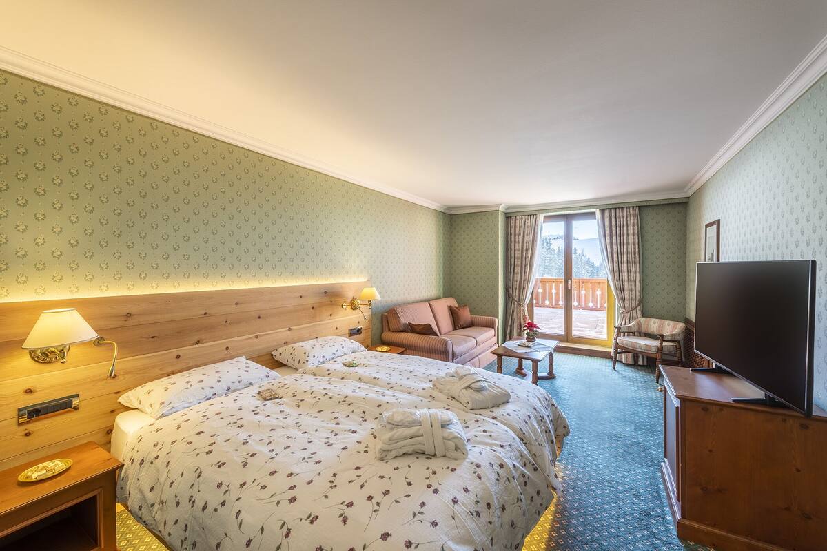 A hotel room with two beds, a sofa, a TV, and a balcony with a view.