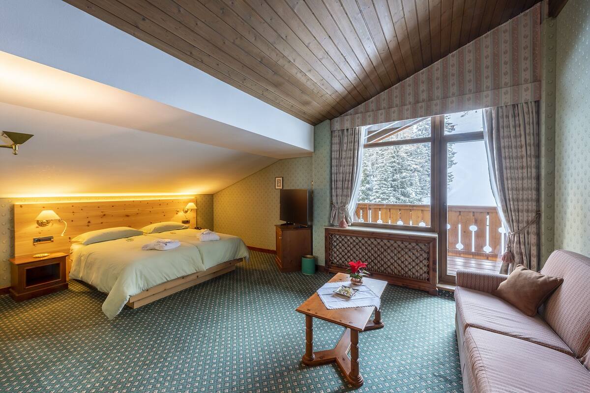 A room with a bed, a sofa, a small table, and a window with a view of trees.