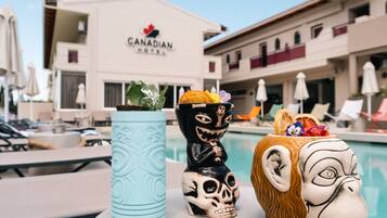 A poolside area with lounge chairs and umbrellas, a Canadian Hotel sign, and decorative items including a skull and a monkey figure.