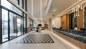 A modern hotel lobby with a checkered floor, a reception desk, and a seating area with a plant. - Canadian (Zakynthos)