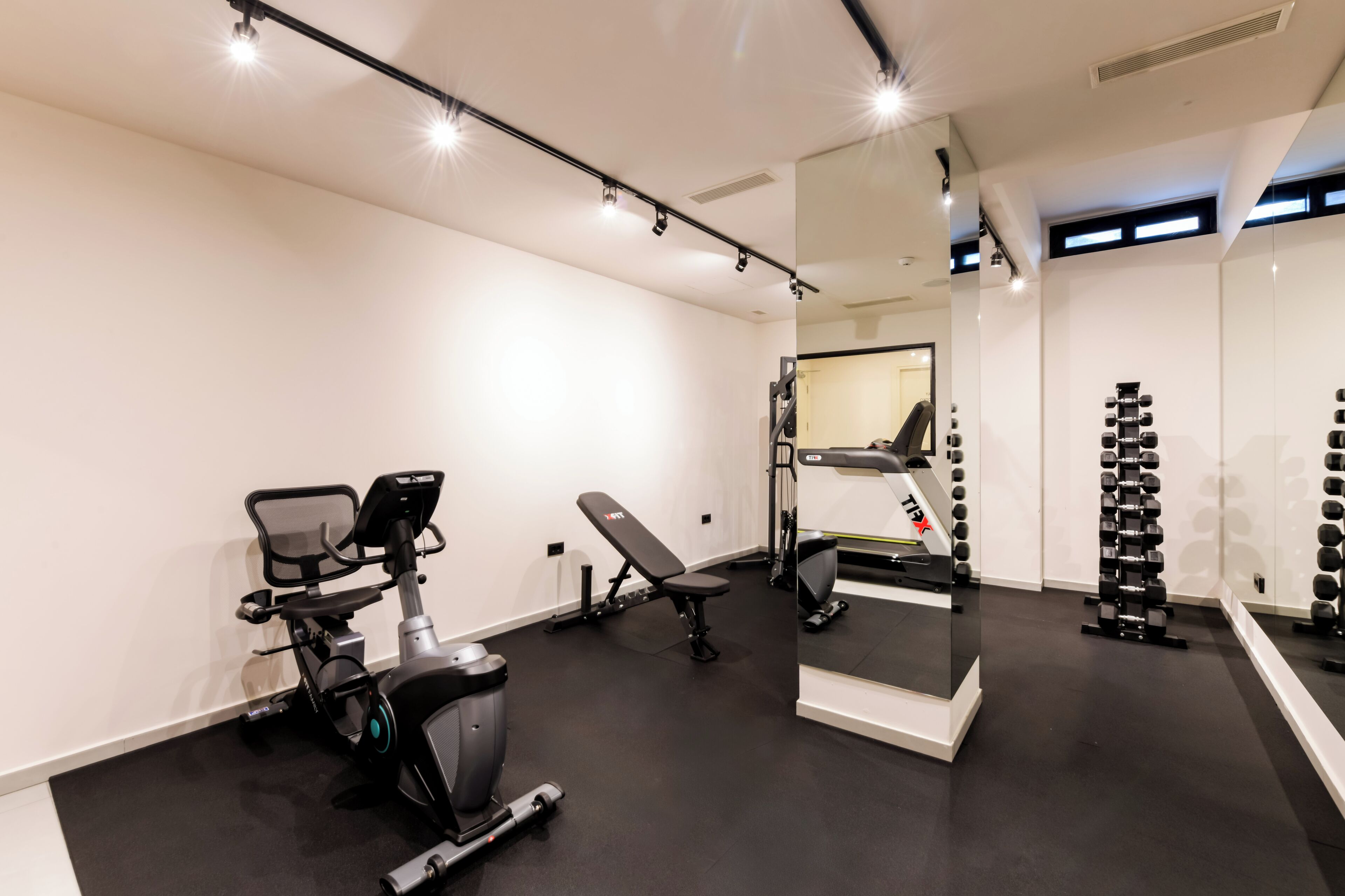 A modern gym with exercise equipment, a mirrored wall, and a clean, minimalist design.