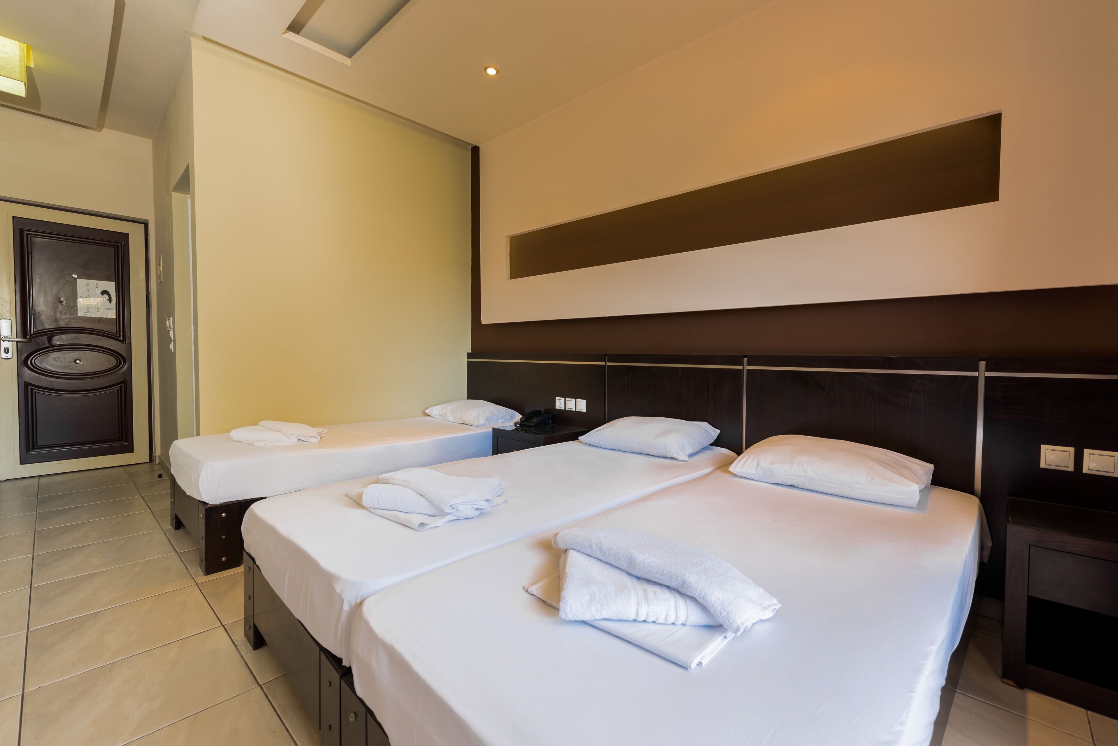 A hotel room with two beds, each with white linens and towels, a dark headboard, and a small bedside table with a phone.