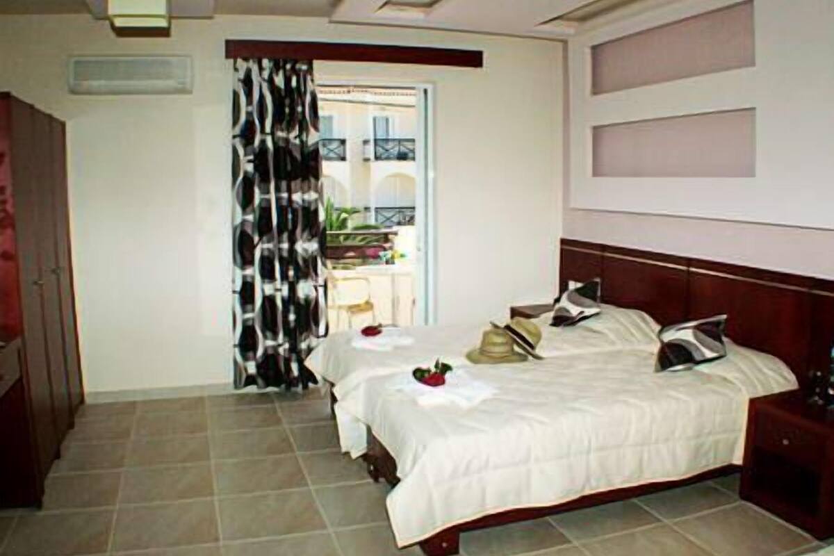 Habitación de hotel con cama, mesitas de noche, armario y vistas al balcón exterior.