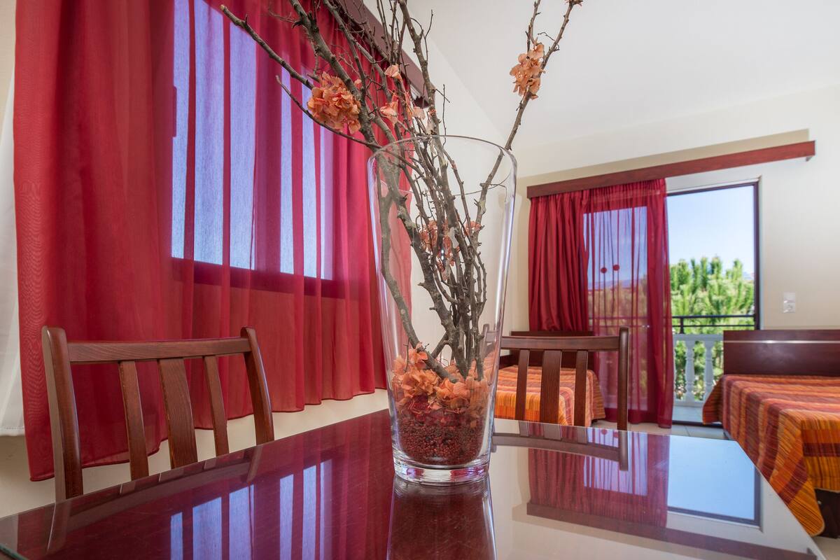 Un comedor con una mesa de madera, sillas y un florero con ramas y flores secas.