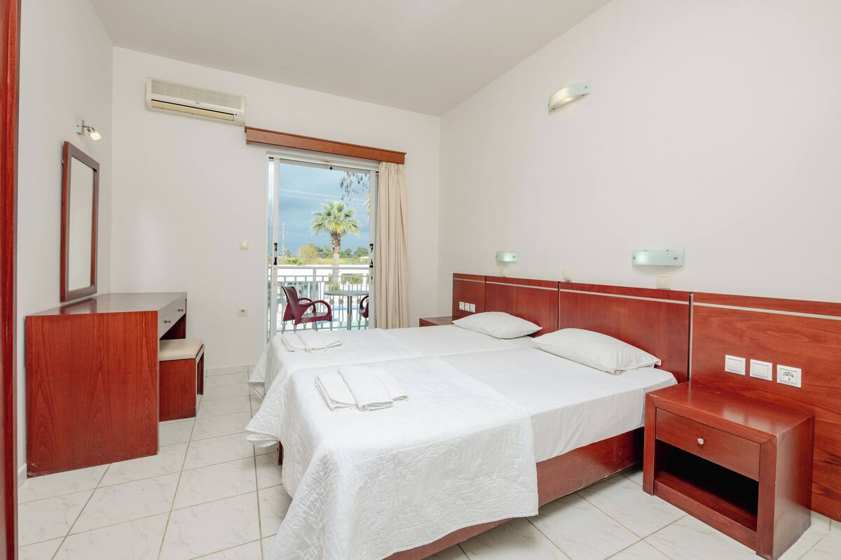 Una habitación de hotel con dos camas, una mesita de noche de madera, un espejo, un escritorio y una silla.
