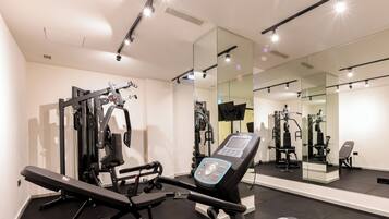 Een sportschool met trainingsapparatuur, een bank en een spiegelwand.