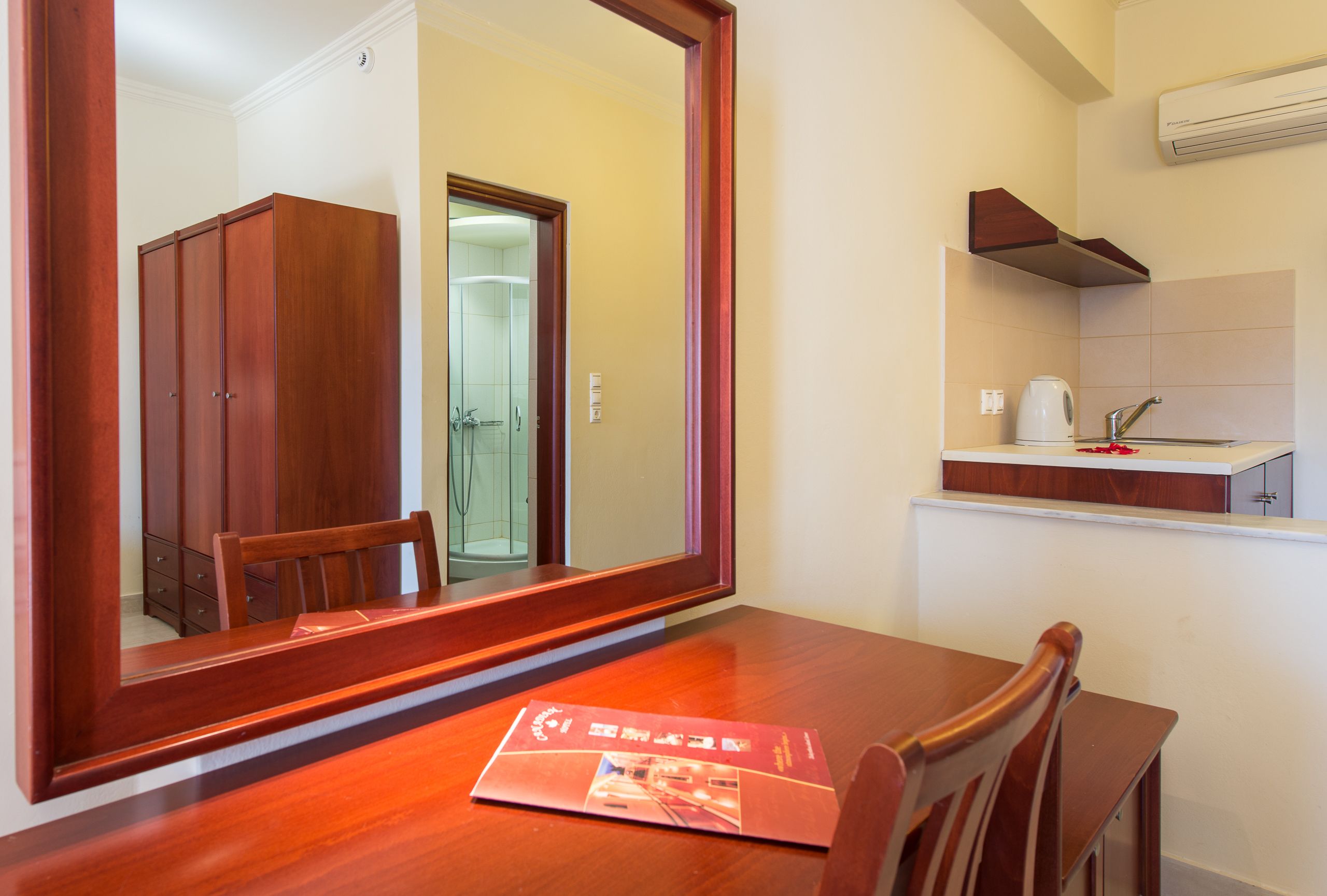 Een houten bureau met een spiegel, een stoel en een tijdschrift. In de achtergrond is een kitchenette te zien met een koffiezetapparaat en een spoelbak.