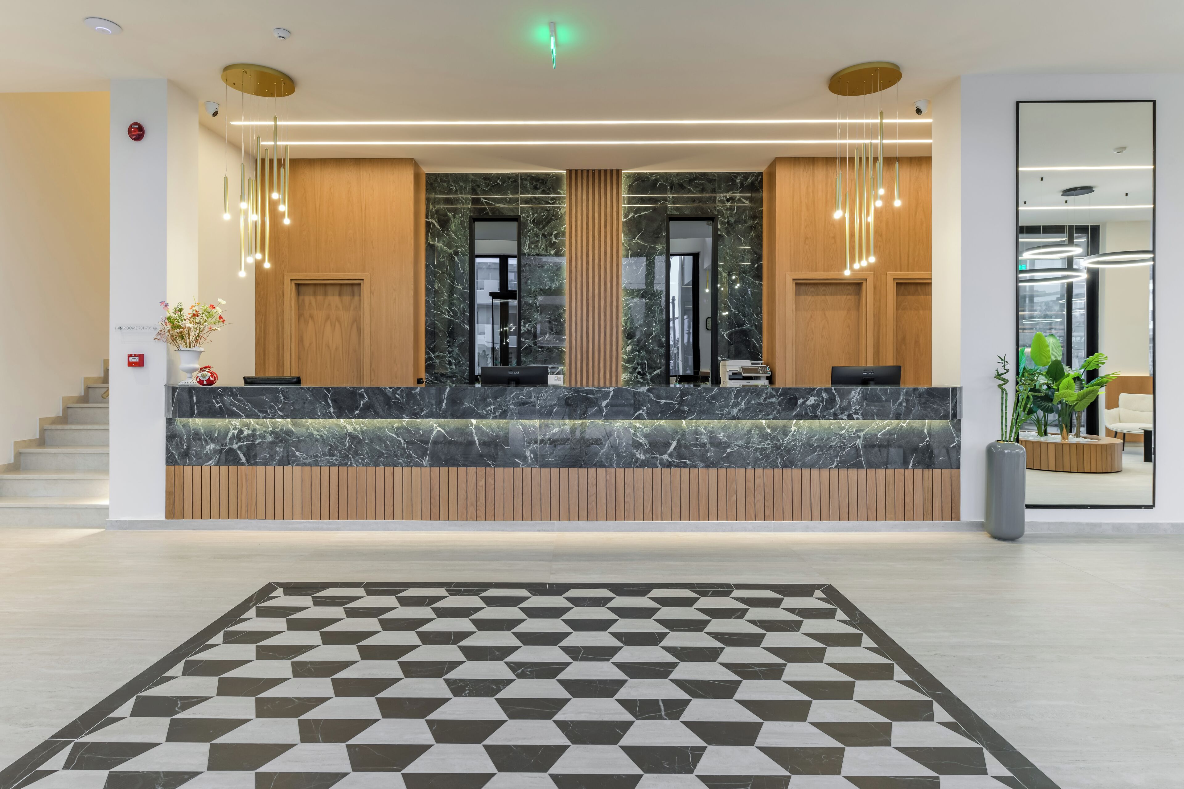 A modern reception desk with marble countertops and wooden paneling, a geometric patterned floor, and a large mirror on the wall.