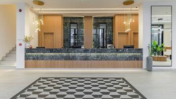 A modern reception desk with marble countertops and wooden paneling, a geometric patterned floor, and a large mirror on the wall.