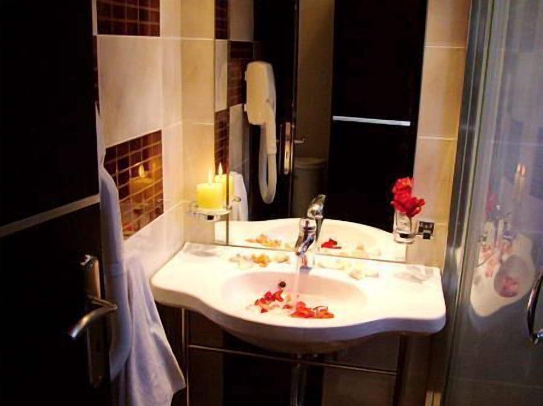 Ein Badezimmer mit einem weißen Waschbecken, einem Spiegel, einer Kerze und einer Duschkabine aus Glas.