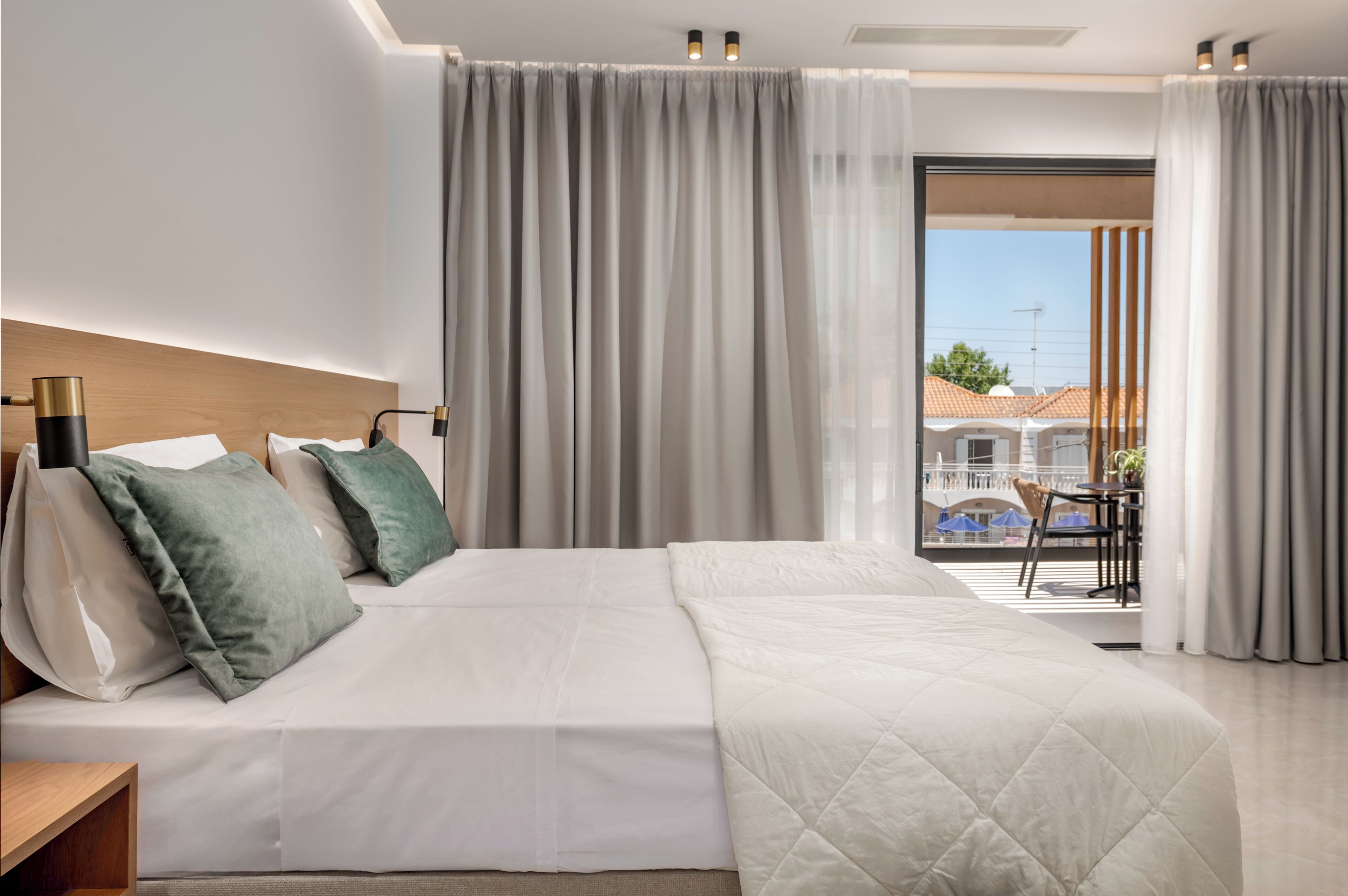 A modern hotel room with a large bed, a wooden headboard, and a balcony with a view of the city.