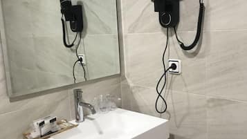 A bathroom with a white sink, a mirror, and a hairdryer mounted on the wall.