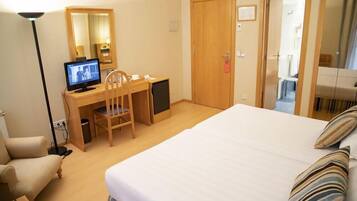 Een hotelkamer met een bed, een bureau met een computer, een stoel, een lamp en een deur.