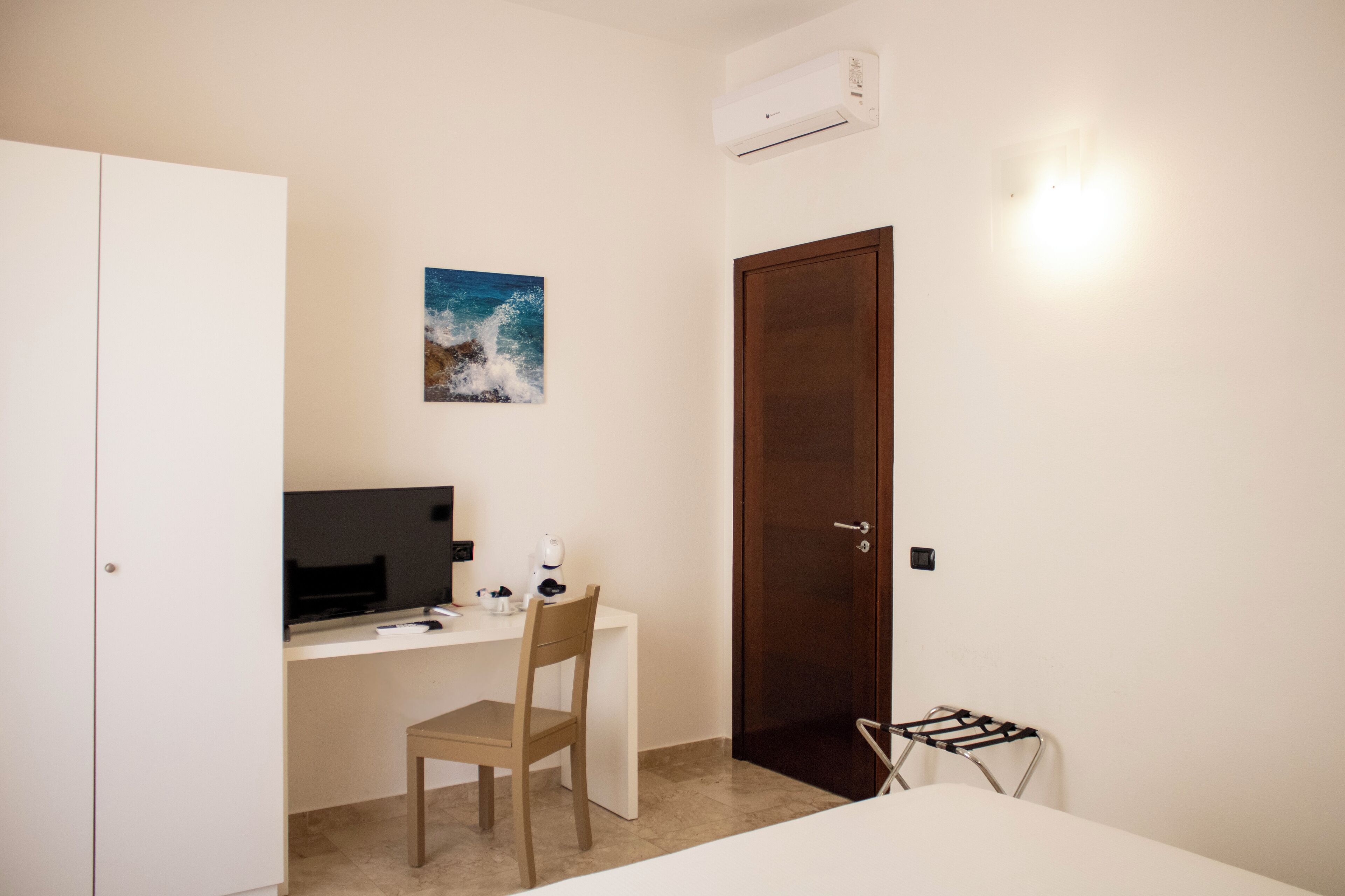 Quarto pequeno com escrivaninha, cadeira e cama.