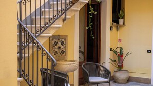 Una escalera con barandillas metálicas decoradas, una fuente de piedra y dos sillas de mimbre cerca de una planta en maceta.