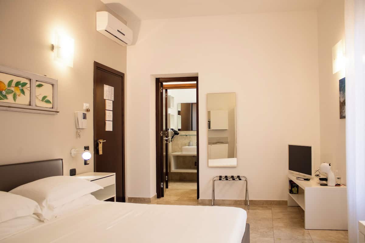 Habitación de hotel con cama, mesita de noche, televisor y baño visible a través de una puerta abierta.