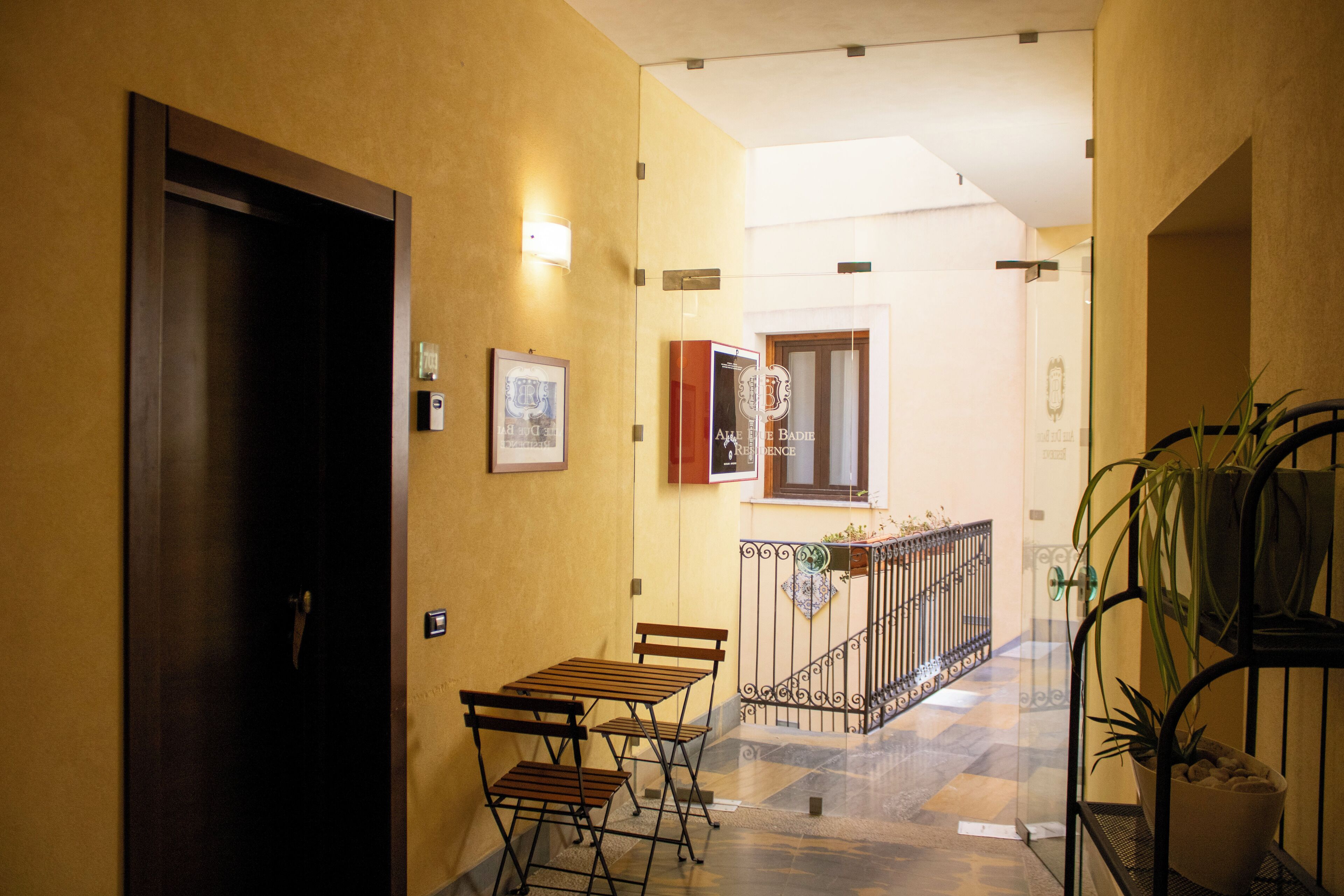 A hallway with a wooden door, a small table with chairs, a potted plant, and a staircase with a metal railing.