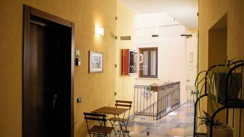 A hallway with a wooden door, a small table with chairs, a potted plant, and a staircase with a metal railing.