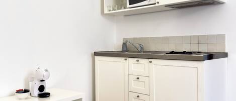 Una cocina con muebles blancos, un microondas y una cafetera en la encimera.