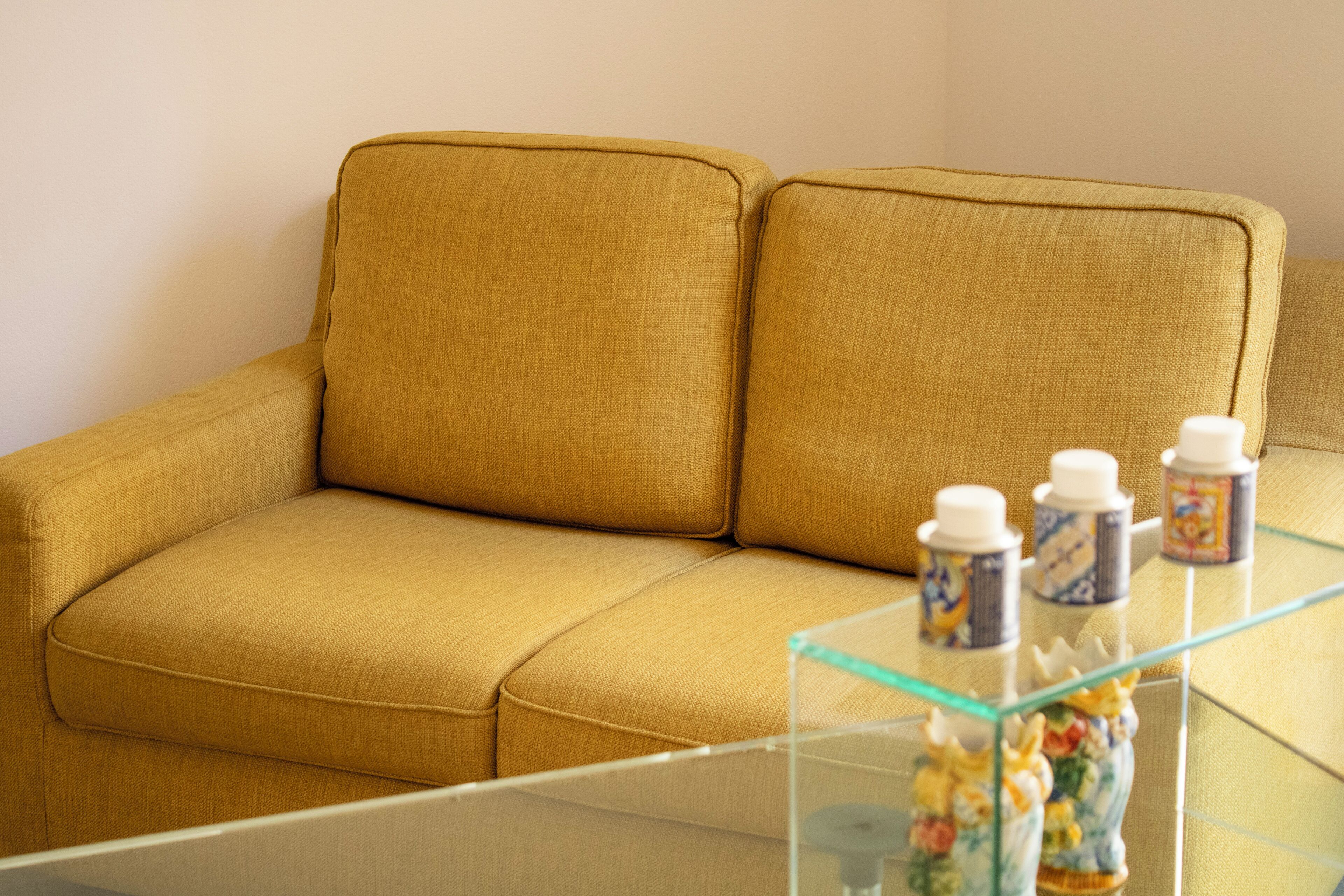 A mustard-colored sofa with a glass coffee table in front.