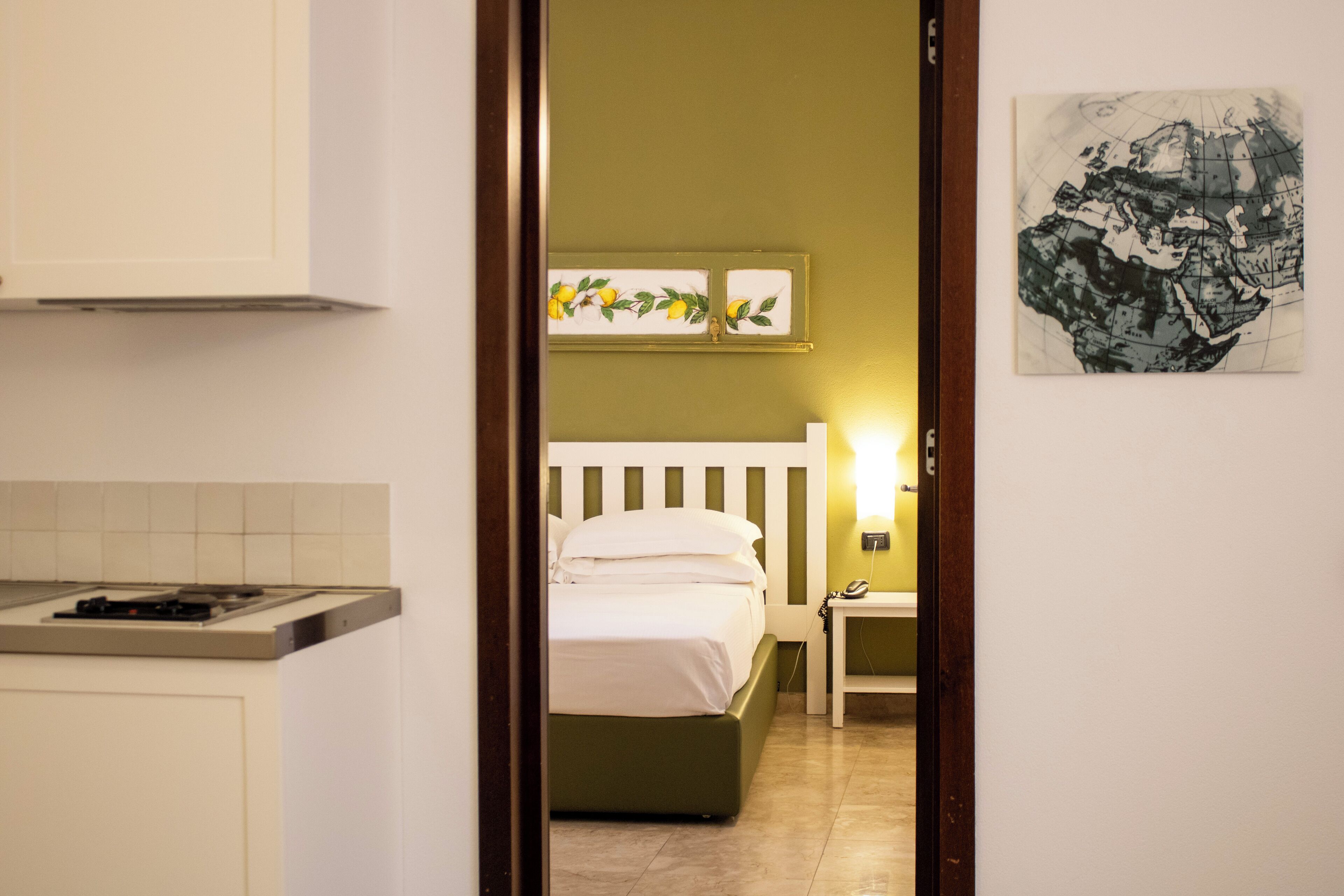 Un pasillo estrecho que conduce a un dormitorio con cama, mesita de noche y una lámpara de pared.