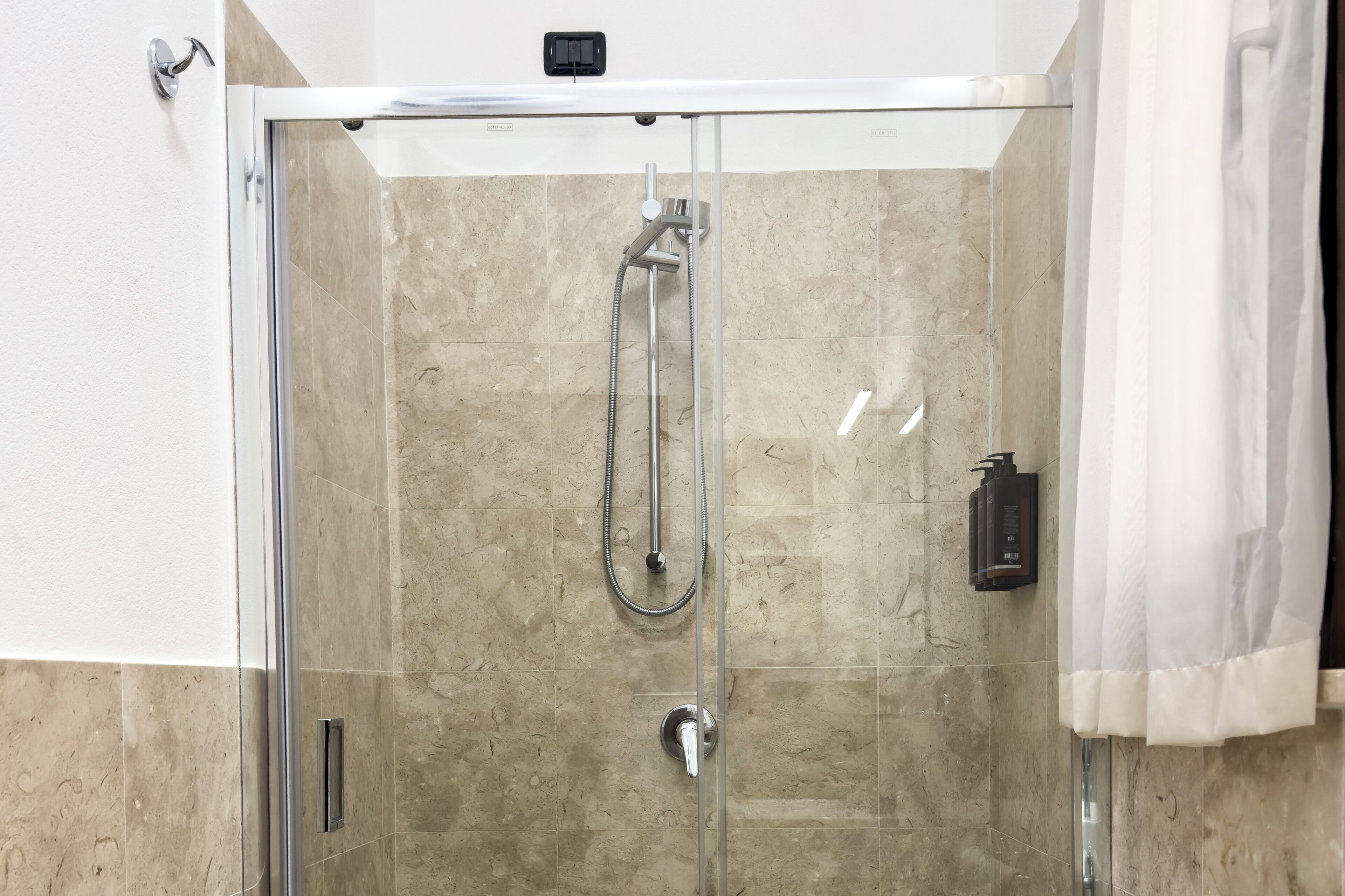 A glass-enclosed shower with a handheld showerhead and a wall-mounted faucet.