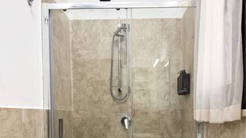 A glass-enclosed shower with a handheld showerhead and a wall-mounted faucet.