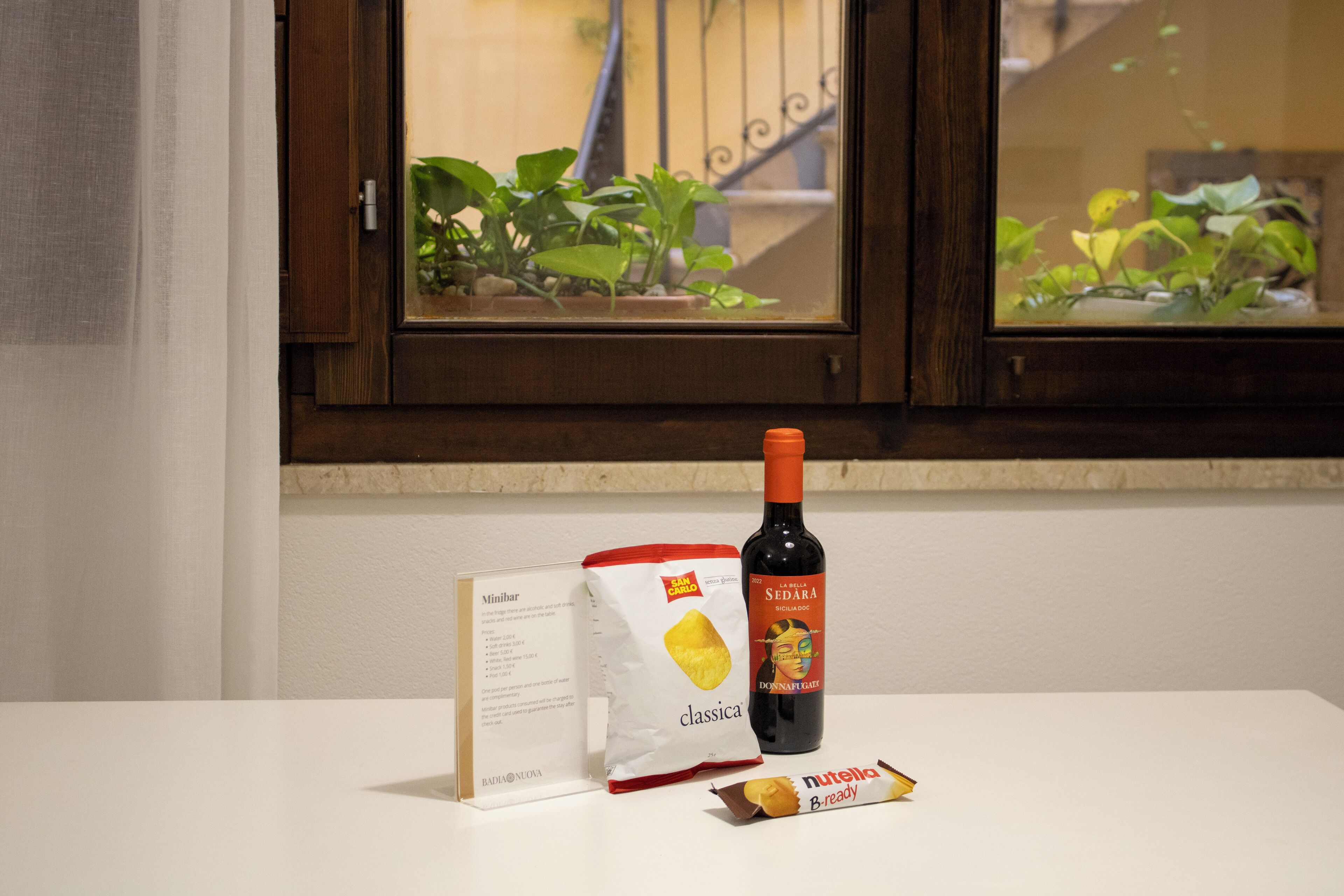Een tafel met een fles wijn, een zakje snacks en een menukaart.