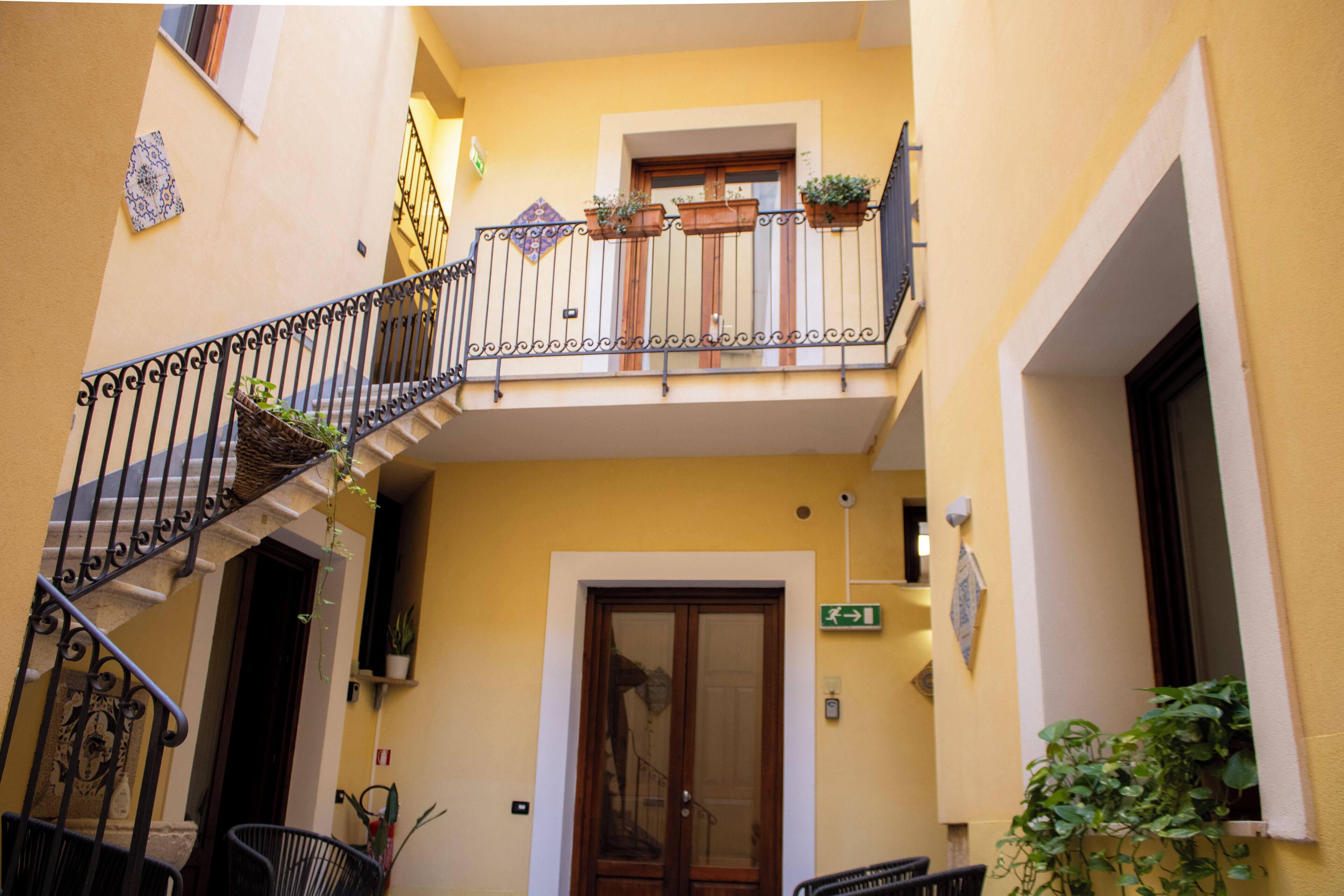 A yellow building with a wooden door, a balcony with potted plants, and a staircase.