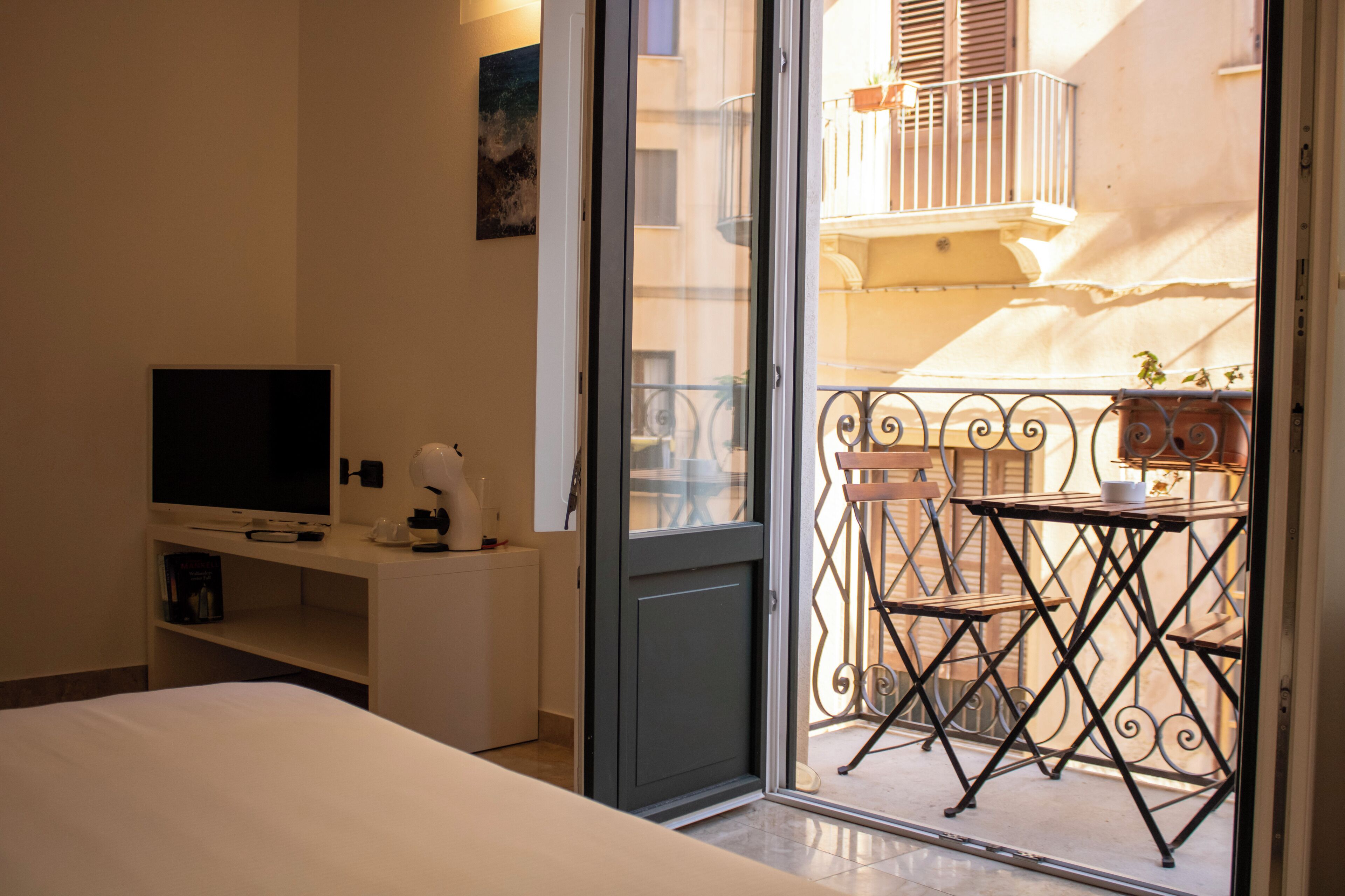 A hotel room with a bed, a desk with a television, a small table with chairs, and a balcony with a railing.
