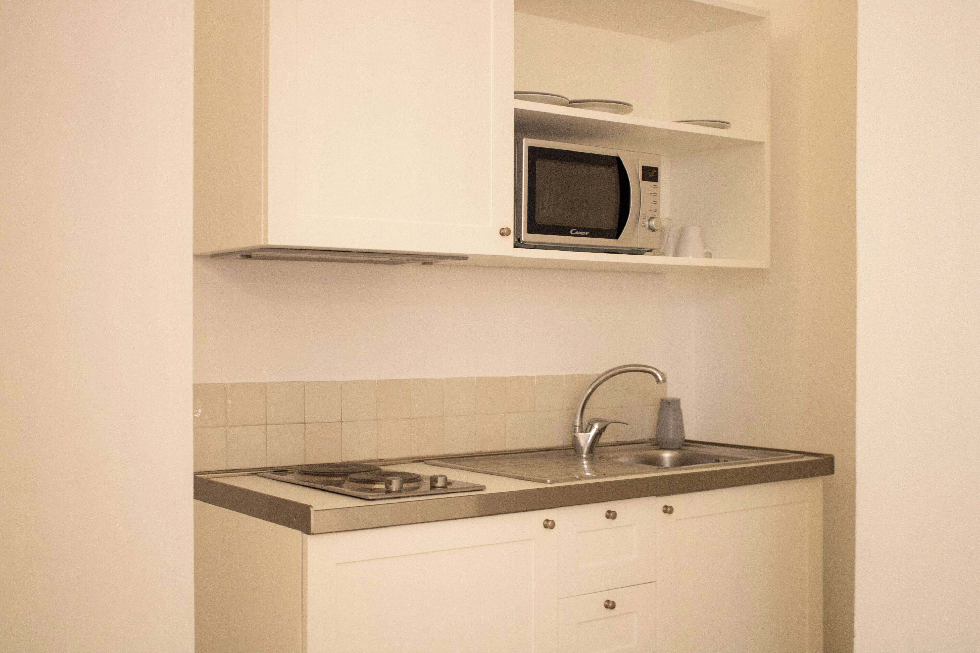 Una cucina compatta con forno a microonde integrato, lavello e piano cottura.