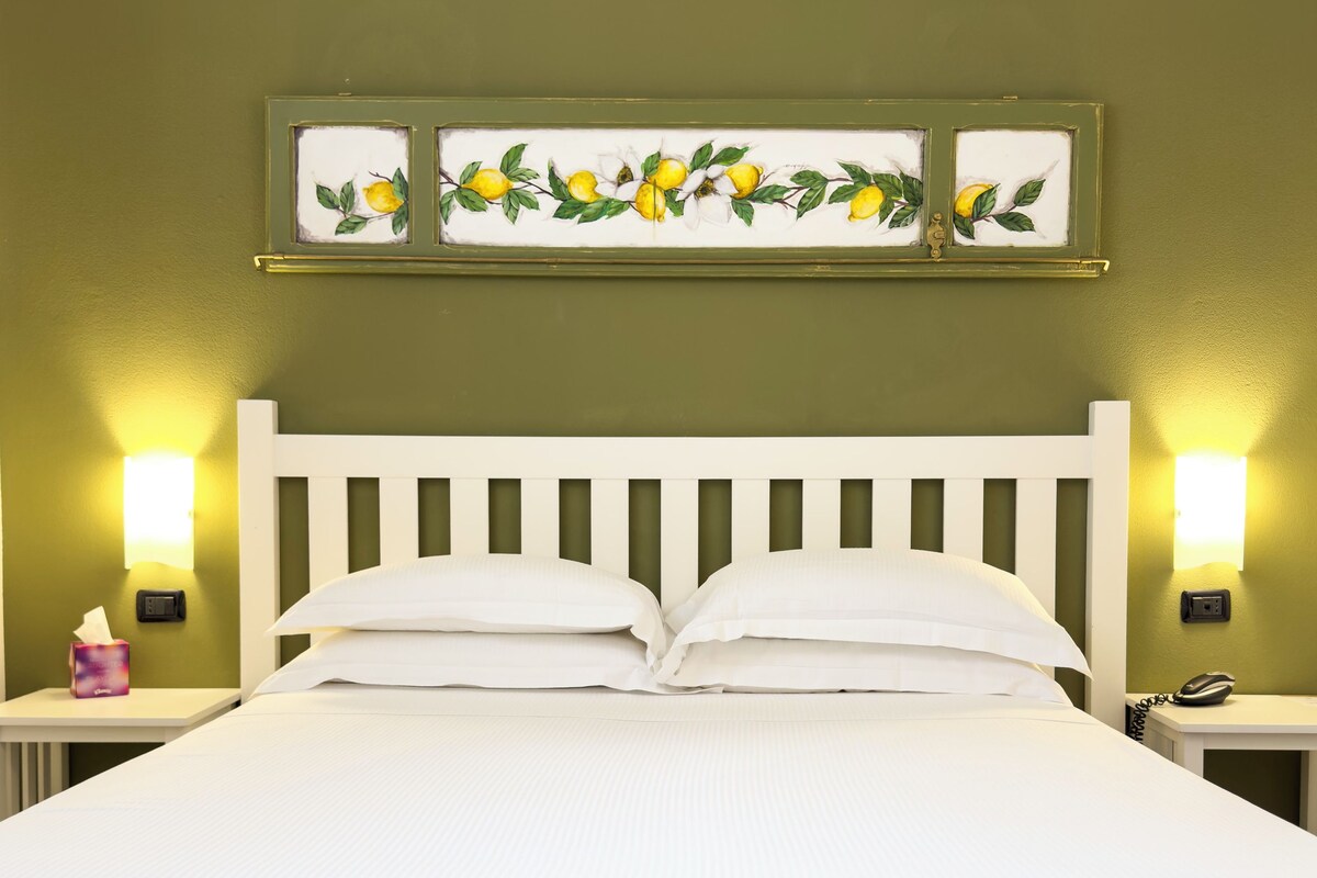 Un lit bien fait, avec du linge de lit blanc, une tête de lit blanche et deux tables de chevet avec des lampes.