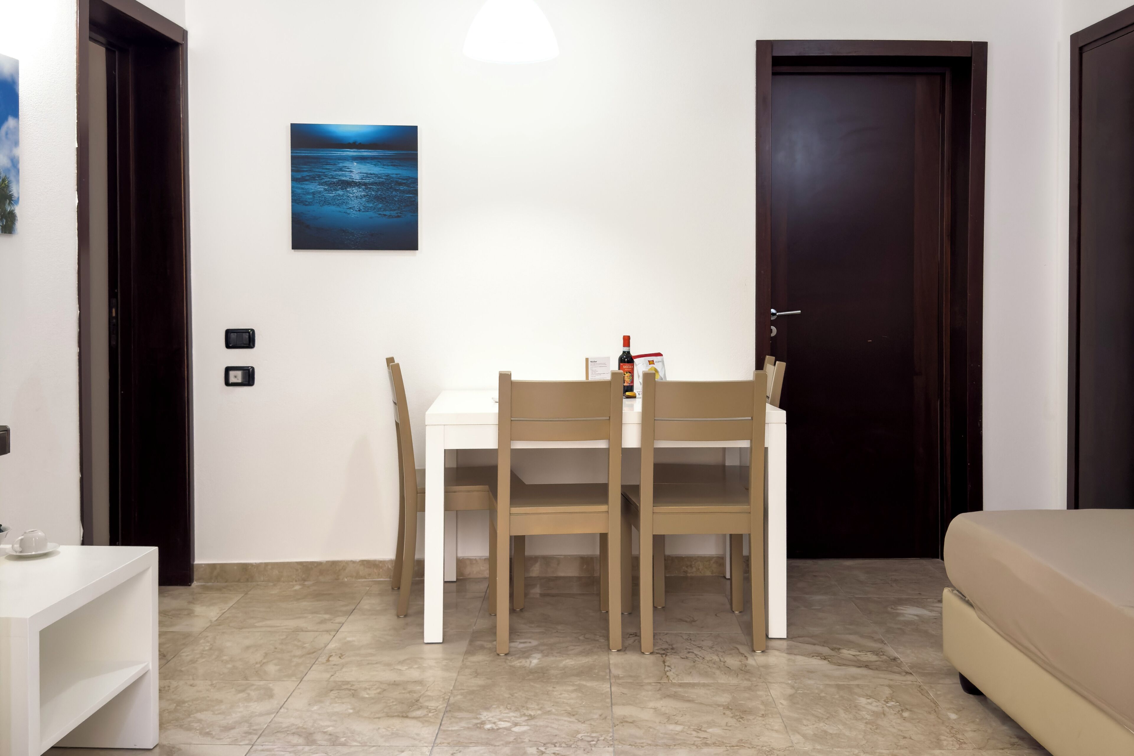 A room with a white table and two chairs, a beige sofa, a dark wooden door, and a framed picture on the wall.